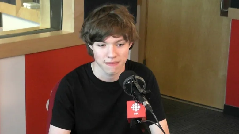 Laef Kucheran, with short hair and a sly expression on his face, sitting behind a microphone with the CBC logo on it. An unfortunately-timed photo.